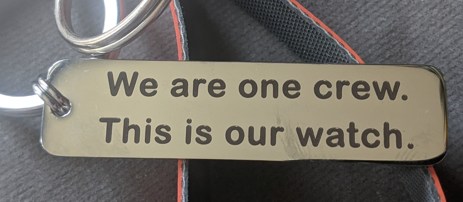 Key ring featuring stainless steel tag reading "We are one crew. This is our watch." and sling made from inshore lifeboat material cut-off.